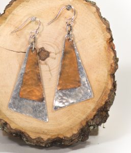 Geometric copper and silver earrings on wood slice