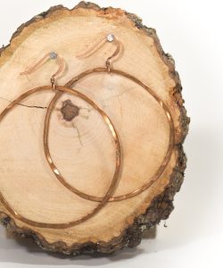 Copper hoop earrings on wood slice background.