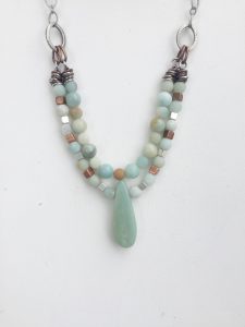 Beaded necklace with aqua pendant on white background.