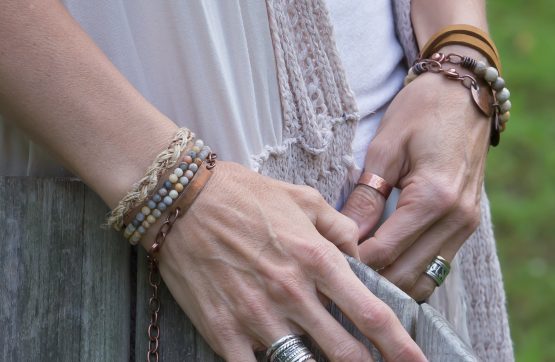 Person wearing multiple bracelets and rings outdoors.