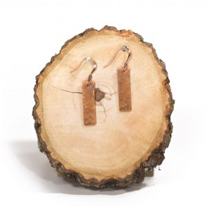 Copper earrings on wooden slice display.
