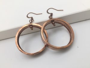 Copper hoop earrings with hooks on white surface.