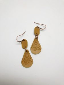 Brown leather earrings with embossed sunburst design.