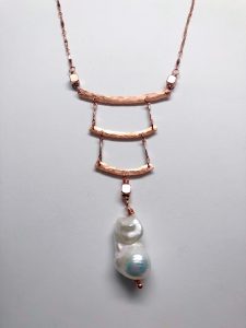 Gold necklace with pearl pendant on light background.