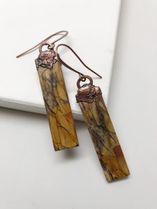 Copper and stone dangle earrings on white surface.