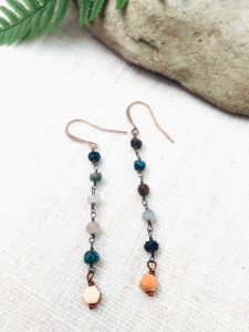 Long beaded earrings with copper accents on white fabric.