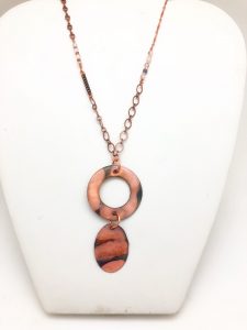 Copper necklace with circular pendants on display bust.