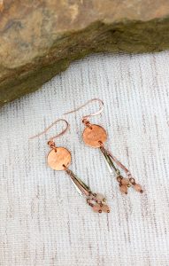 Copper and bead dangle earrings on woven fabric.