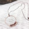 Copper circle necklace with beaded accents on fabric.