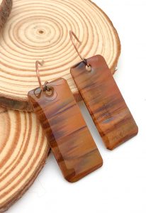 Brown rectangular earrings on wooden background.