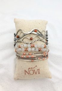 Stacked bracelets on cushion with beach sand background.