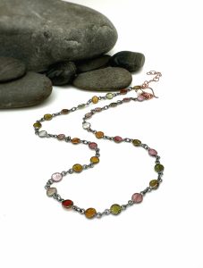 Colorful gemstone necklace on smooth gray stones.