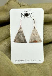 Handmade triangular metal earrings on fabric background.
