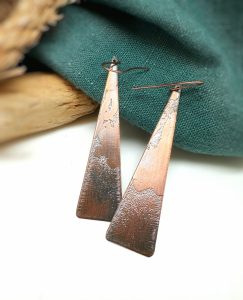 Copper triangle earrings on green fabric.