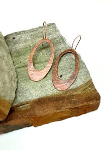 Copper oval earrings on textured stone slab.