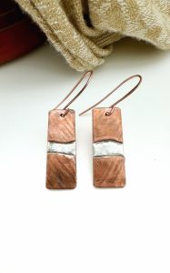 Copper and silver dangle earrings displayed on fabric.